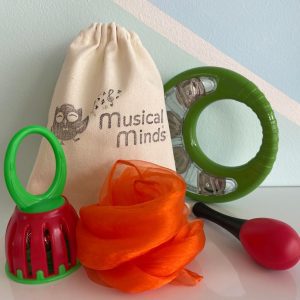 A baby musical instrument pack including a canvas Musical Minds bag, a green and red bell shaker, an orange sensory scarf, a green tambourine, and a red maraca