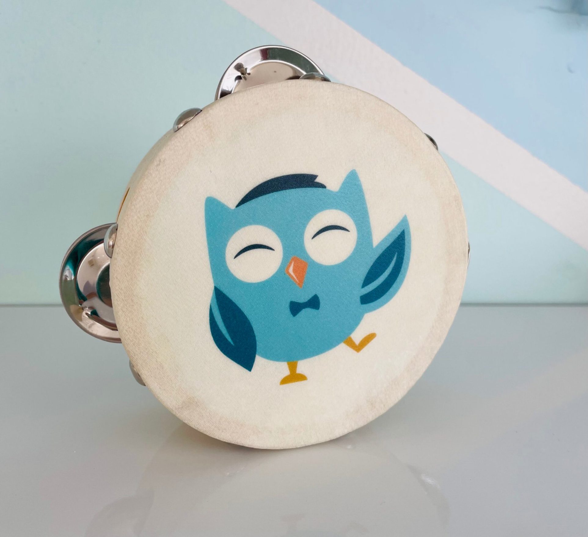 A close-up of a small wooden tambourine featuring an illustration of a blue owl